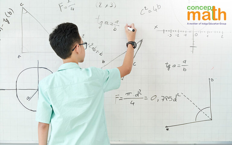 A young male student writes math equations on a whiteboard.