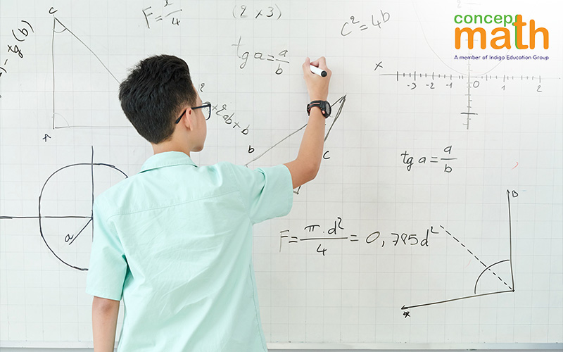 A young male student writes math equations on a whiteboard.