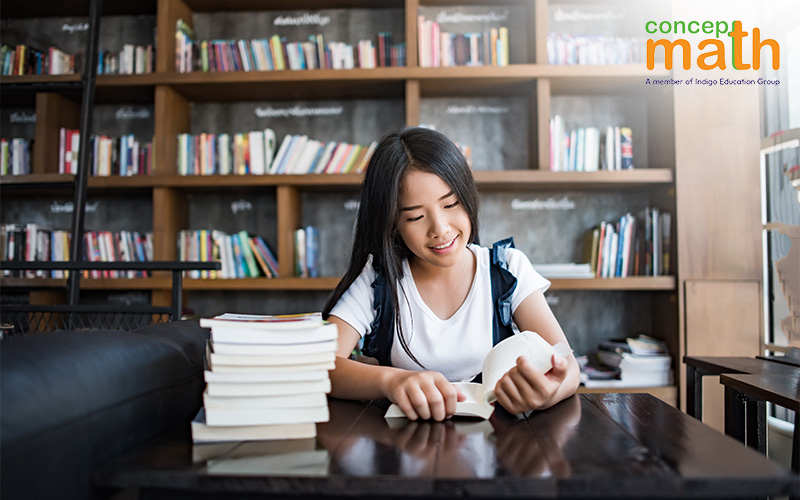 A young woman smiles while reading a book in a library.