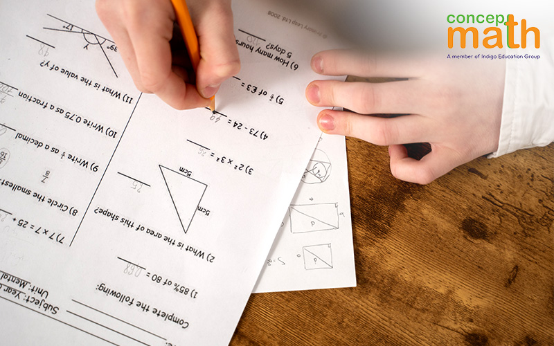 Close-up of hands writing answers on a math worksheet with various problems.