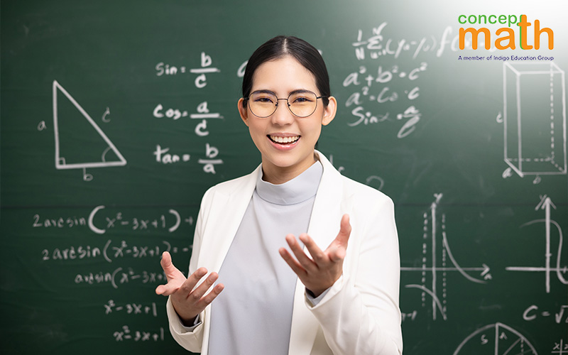 A smiling female teacher stands in front of a blackboard covered in math formulas.